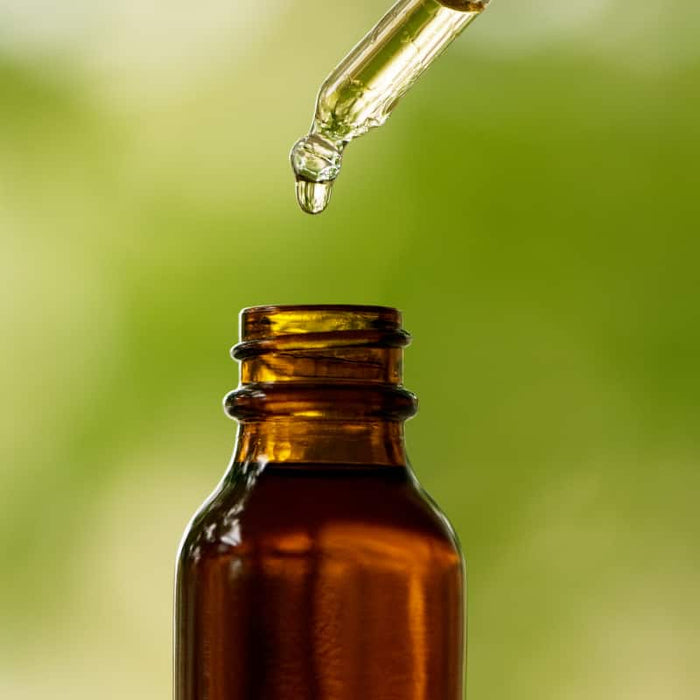 Close-up of a dropper releasing a golden liquid drop into an amber glass bottle, showcasing Bath & Body Oil | Privai for natural skincare and body care routines.