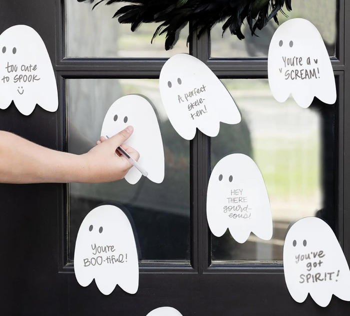 Hand placing a white ghost-shaped sign with text on a window, surrounded by similar ghost signs.