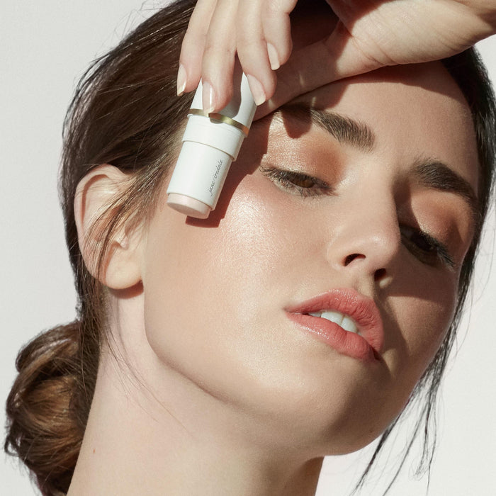 Woman applying Glow Time Highlighter Stick | Jane Iredale to her cheek, highlighting radiant, glowing skin in natural light.