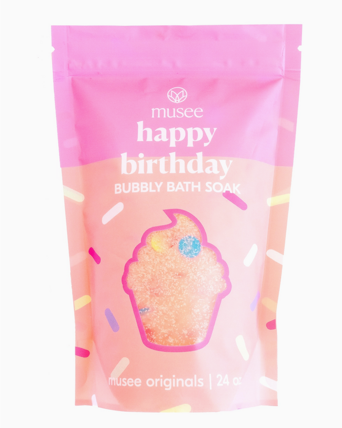A pink package labeled 'Musee happy BIRTHDAY bubbly bath soak' with an image of a cupcake and sprinkles, indicating the product scent.