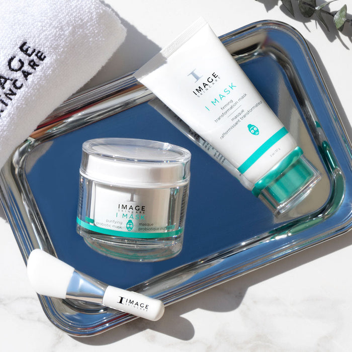 I MASK purifying probiotic mask | IMAGE Skincare displayed in jars and tubes on a reflective tray with an applicator brush and a white towel, highlighting skincare and wellness.