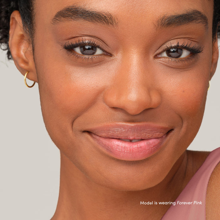 Close-up of a smiling woman with natural makeup highlighting soft pink lips and cheeks, showcasing the effect of Just Kissed Lip And Cheek Stain | Jane Iredale.