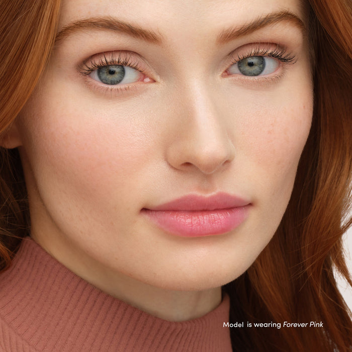 Close-up of a woman with clear skin and natural makeup highlighting soft pink lips and cheeks, showcasing Just Kissed Lip And Cheek Stain | Jane Iredale in Forever Pink.