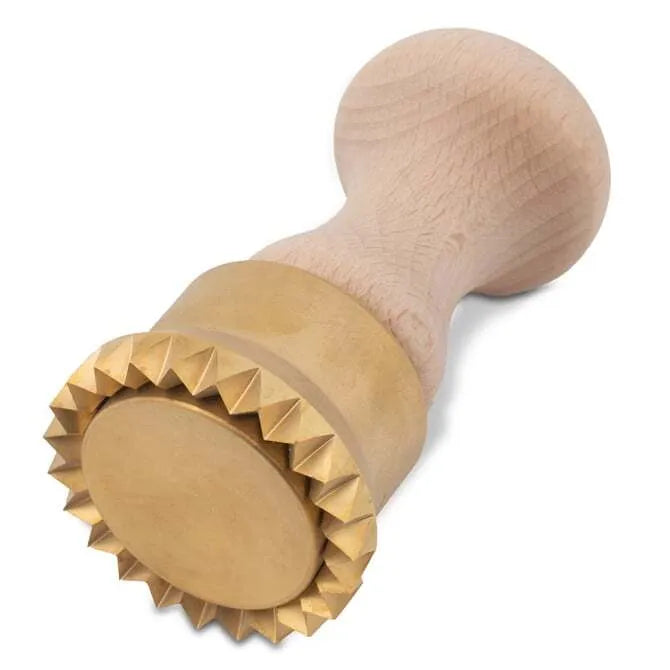 A wooden handle pasta stamp with brass components, featuring apparent flaws as part of its artisan production on its side on a white background.