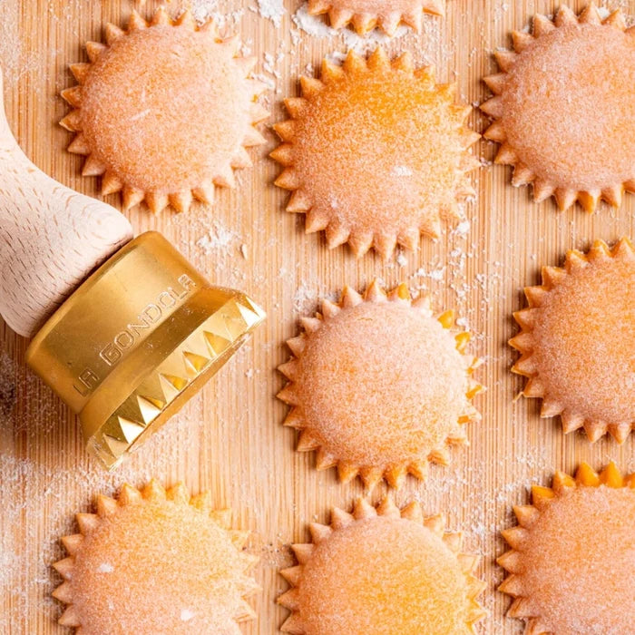 Decorative pasta stamp on a wooden surface with fresh round pasta shapes on wooden table.