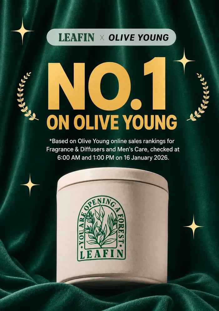 A promotional graphic for a LEAFIN x OLIVE YOUNG fragrance product. A cream-colored cylindrical tin with a green LEAFIN logo sits on draped dark green fabric, surrounded by gold starbursts and laurel wreaths.