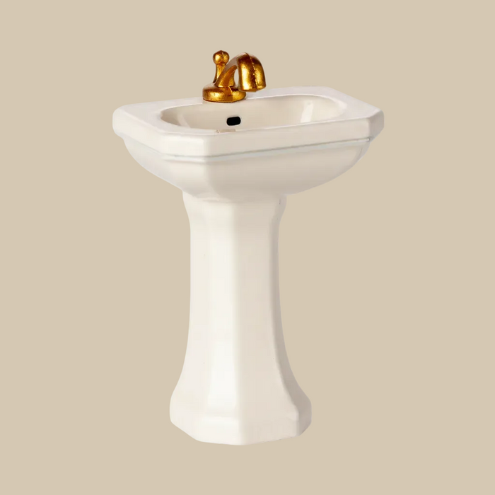 Pedestal sink with gold faucet on a white background