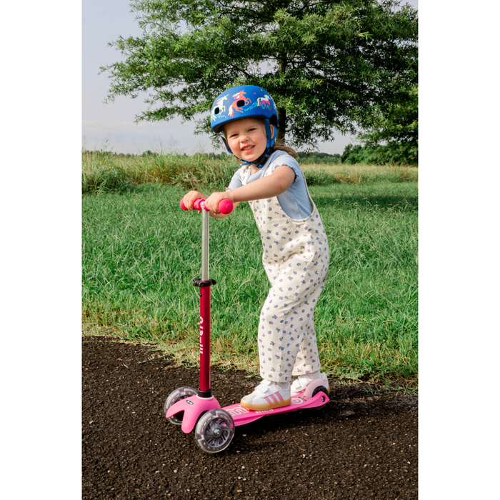 Child on a pink scooter wearing a helmet in a grassy outdoor setting