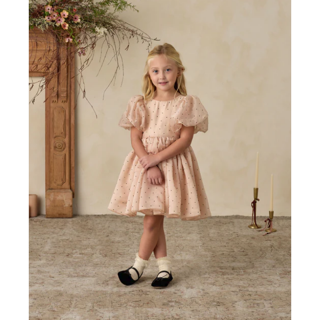 Young girl in a pink dress standing in a room with decorative elements.