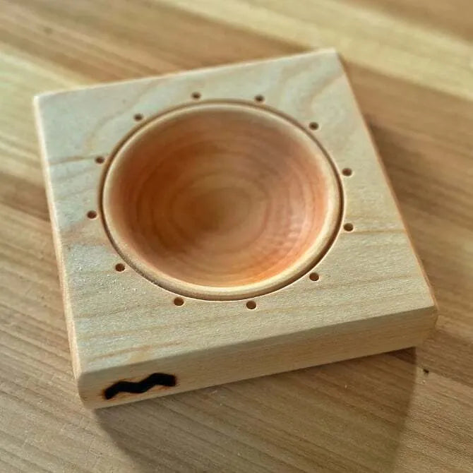 A square maple wood ravioli mold with a circular indentation in the center, placed on a wooden surface.