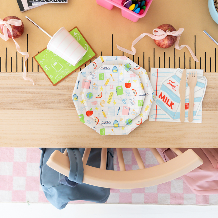 Children's table setting with colorful plate, napkin, and cutlery on a wooden table.